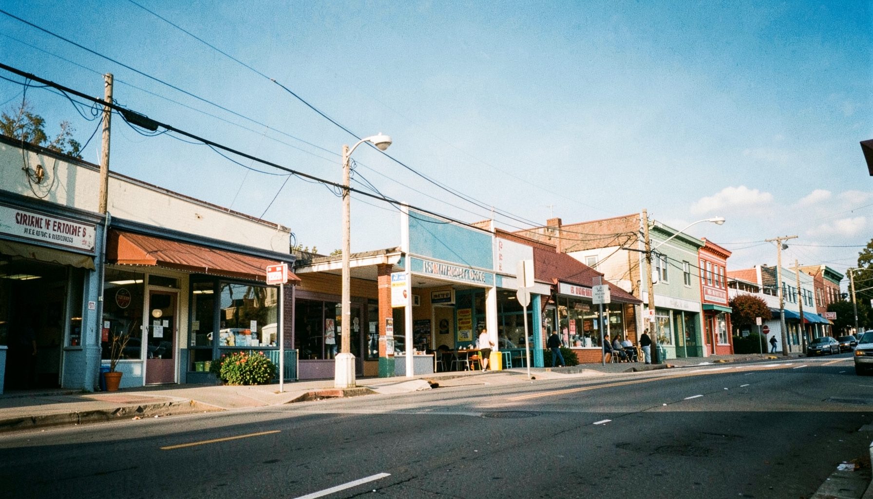 A wide view of a Rockaway street scene with storefronts and community buildings under a bright sky, warm and inviting