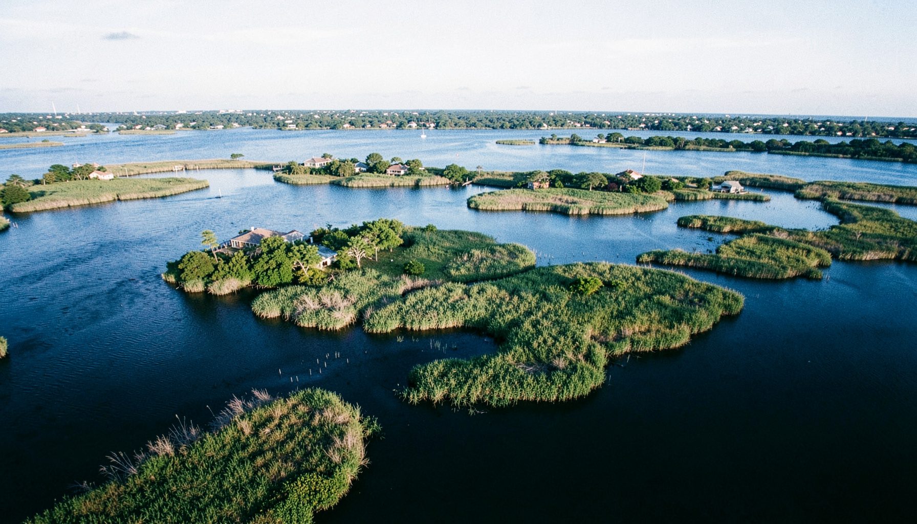 Aerial view of Jamaica Bay marshlands with Broad Channel island homes nestled among green reeds and calm blue water under soft afternoon light